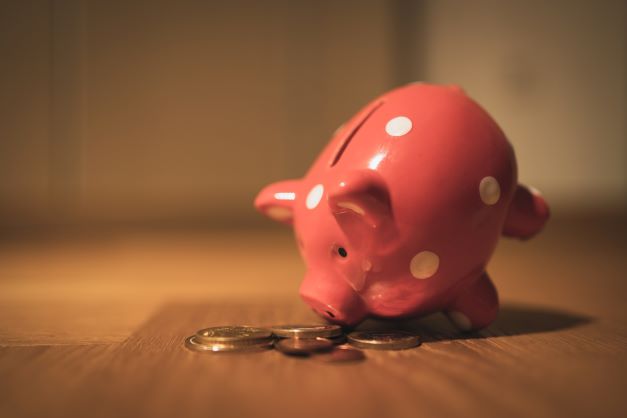 a pink piggy-bank on its side next to a pile of coins to represent a money saving